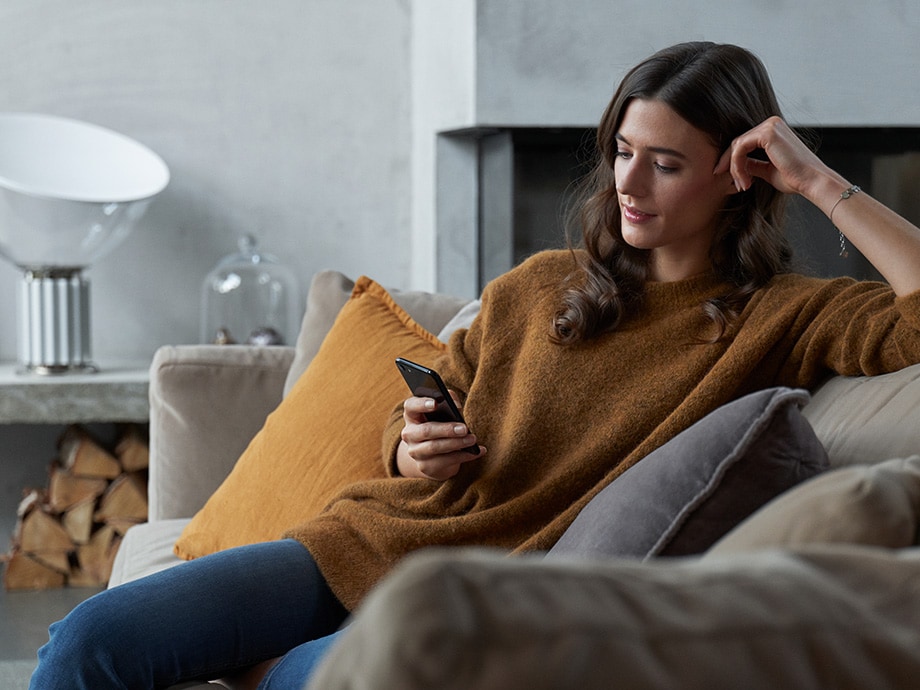 Kvinna som sitter på soffan och tittar i sin mobiltelefon