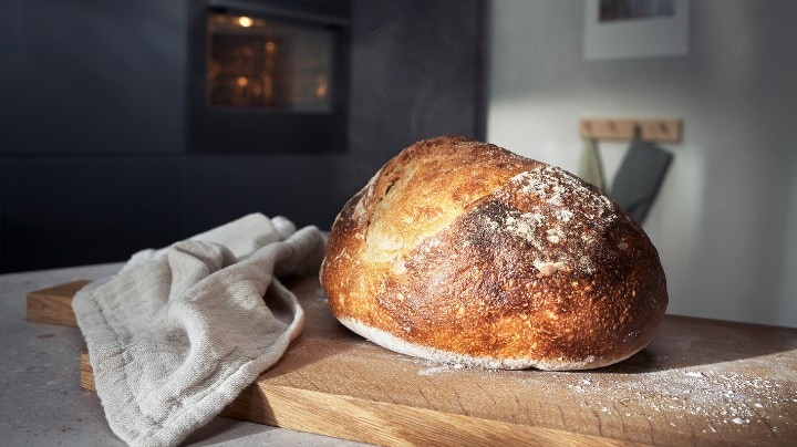 Ett nybakt bröd ligger upplagt på en skärbräda. I bakgrunden syns en ångugn från Electrolux.